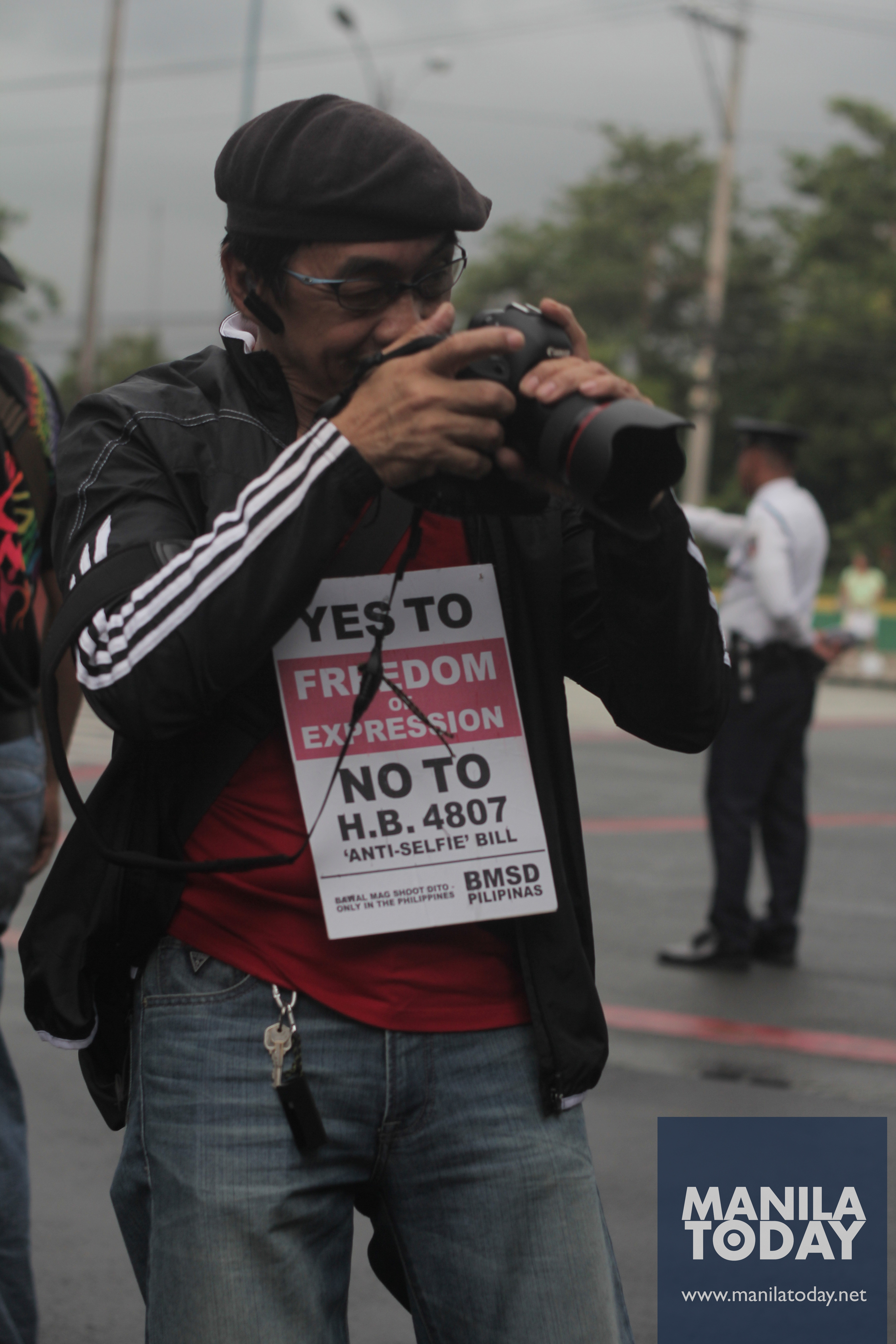A photographer checks on his camera with a card against House Bill 4807 is hanged on his neck.